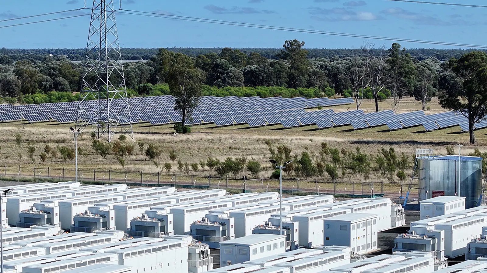 Rows of Battery Energy System enclosures beside a solar farm and transmission line, Western Downs QLD